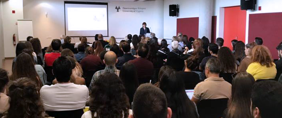 Photo of a room full of people looking at a speaker with a presentation in the background